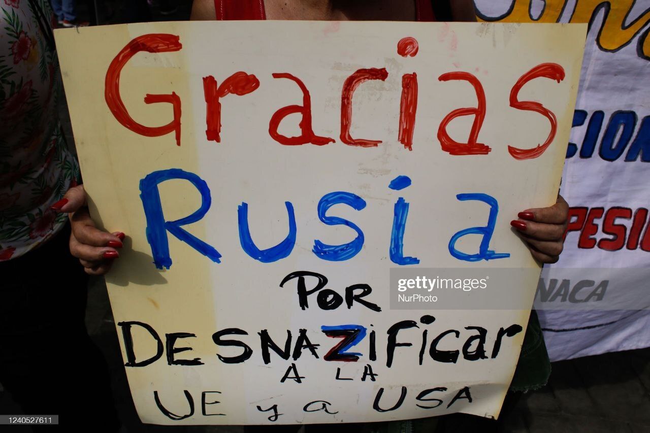 Женщина с плакатом "Спасибо России за денацификацию ЕС и США" во время церемонии шествия "Бессмертного полка" в Каракасе, Венесуэла.